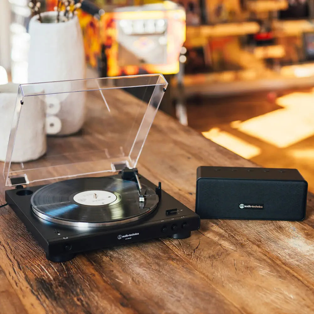 Tornamesa Automática AT-LP60XBT reproduciendo un disco y Altavoz Bluetooth AT-SP65XBT 