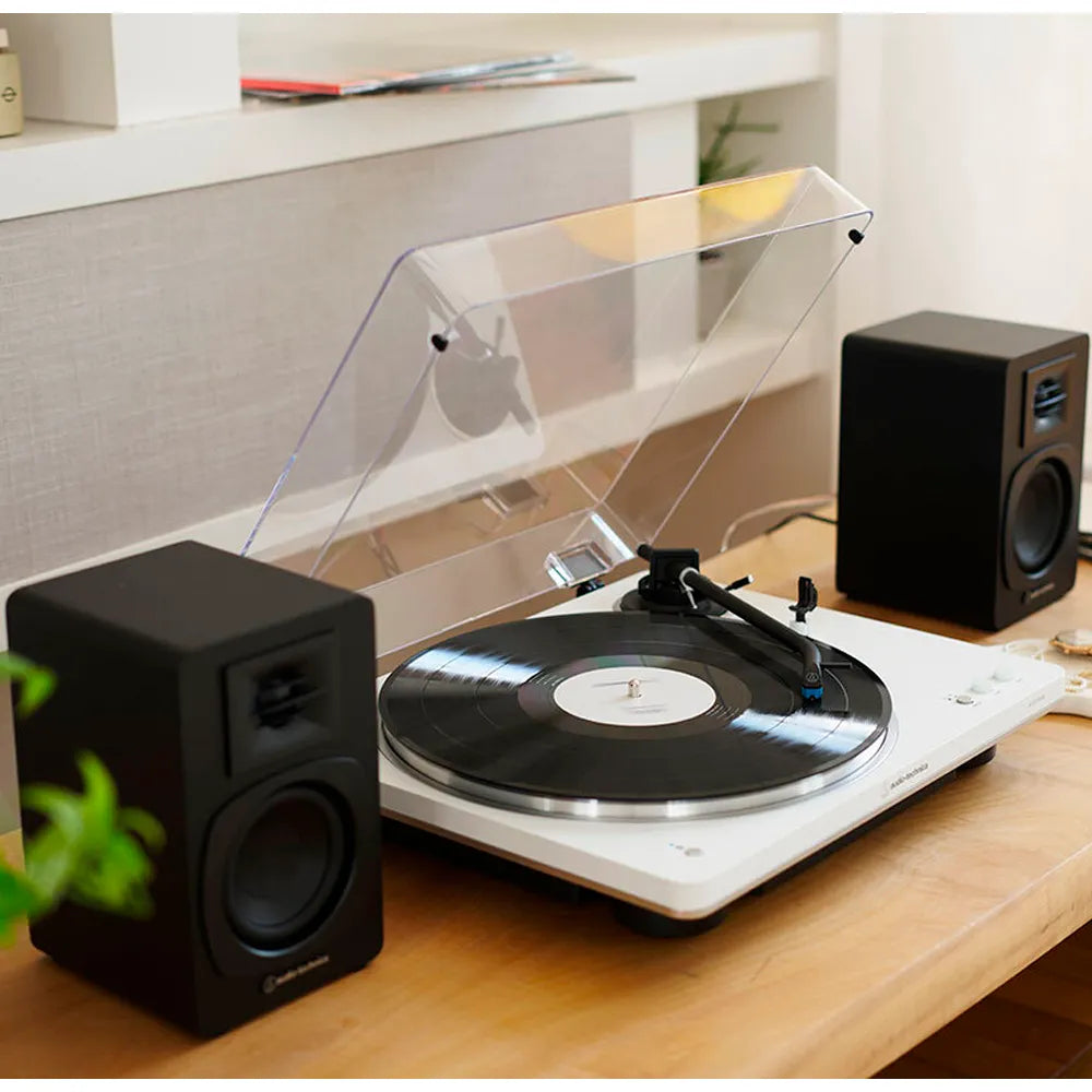 Tornamesa Automática AT-LP70XBT blanca y Altavoces Bluetooth AT-SP3X negros en un escritorio
